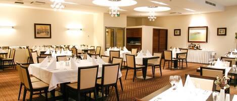A hotel dining area with round tables, chairs, and chandeliers.
