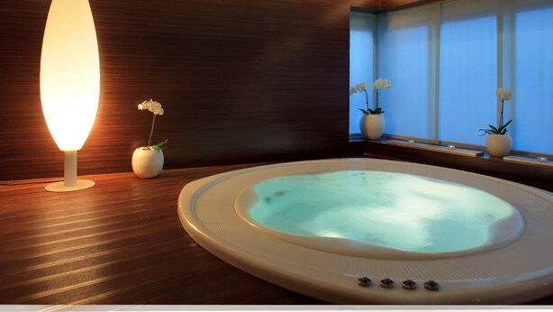 A modern spa room with a hot tub, wooden paneling, and potted orchids. - Hotel Aristos (Zagreb)