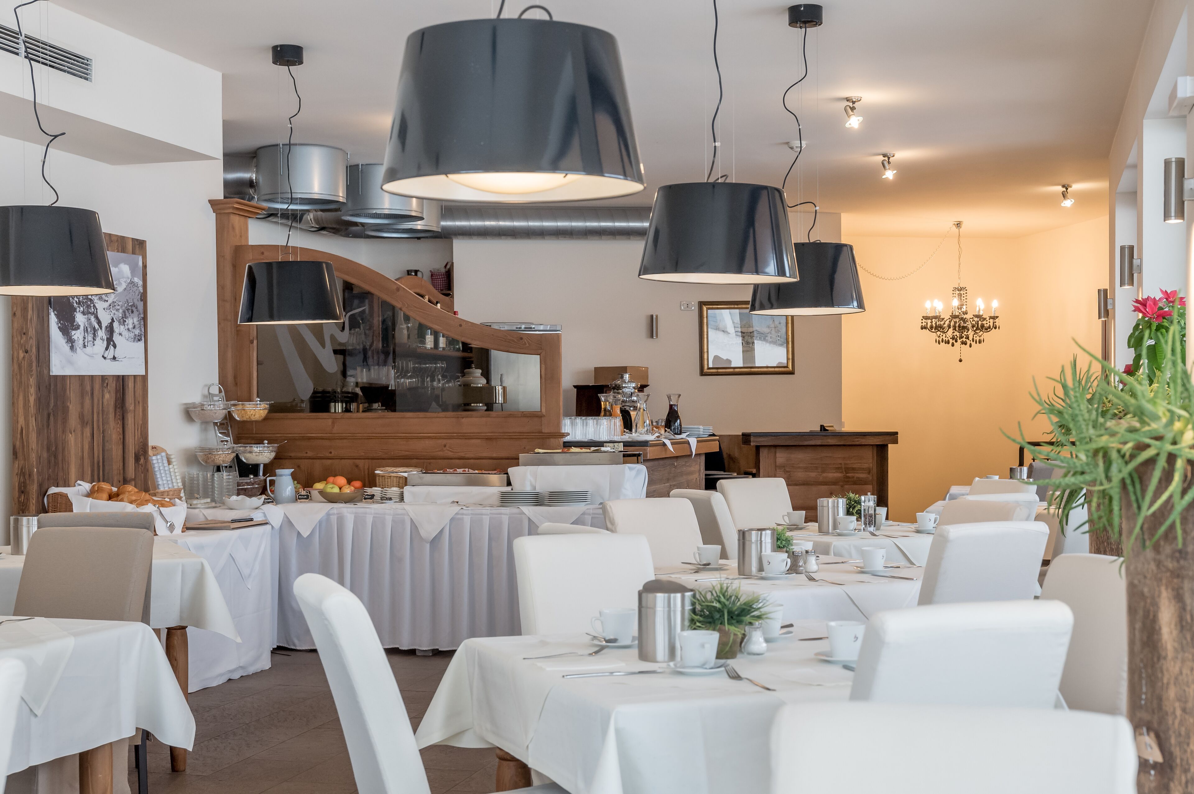 Een eetruimte met gedekte tafels, een houten trap en een keuken op de achtergrond.