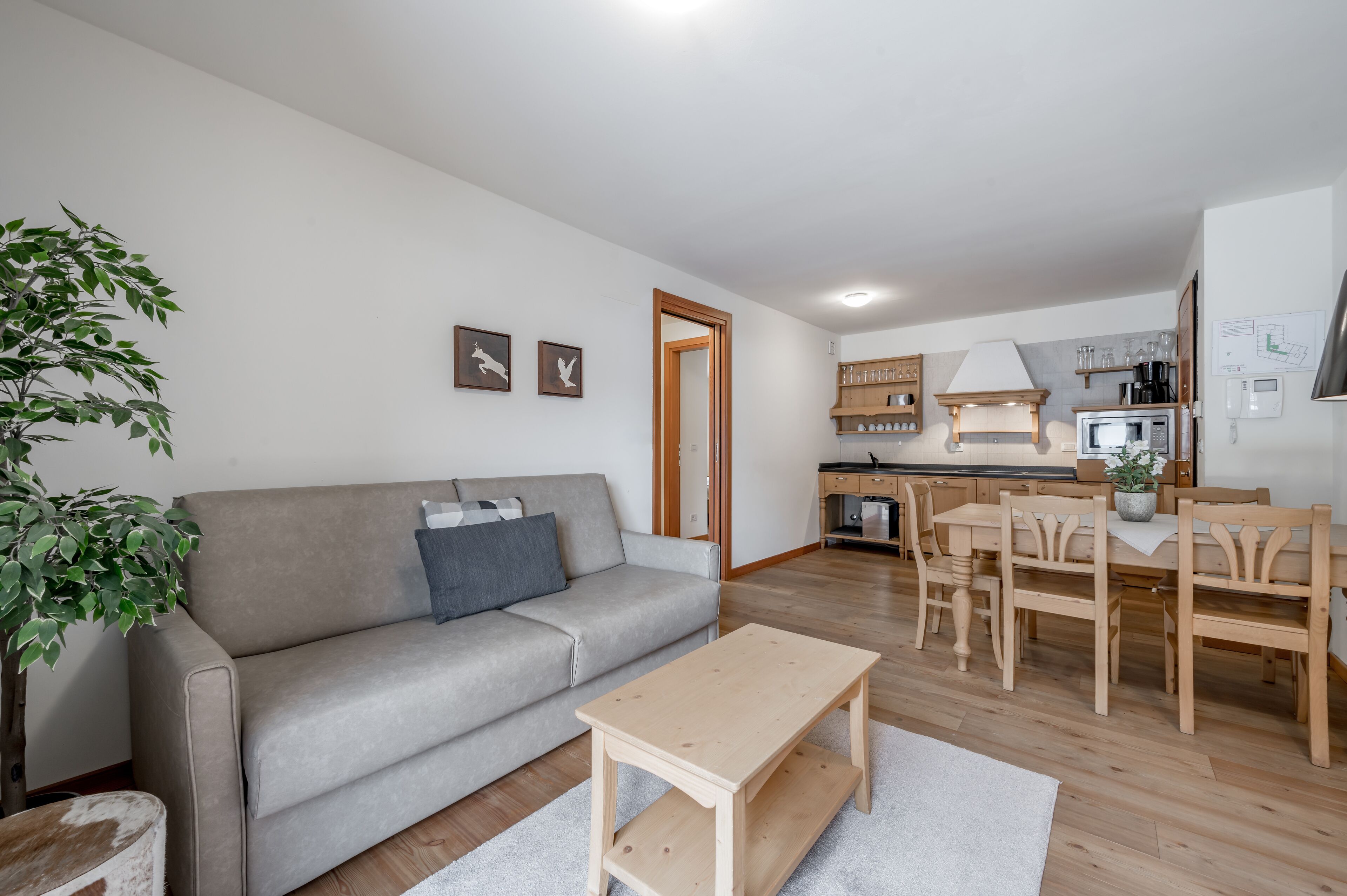 Una sala moderna con un sofá gris, una mesa de centro de madera y una zona de comedor con una mesa y sillas de madera.