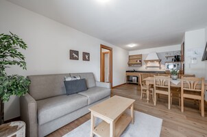 Una sala moderna con un sofá gris, una mesa de centro de madera y una zona de comedor con una mesa y sillas de madera.
