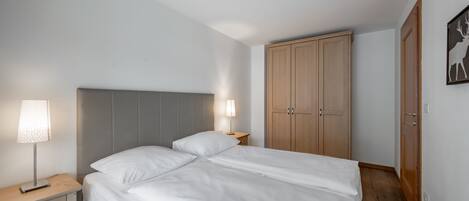 A bedroom with a double bed, bedside tables with lamps, a wardrobe, and a door with a deer artwork.