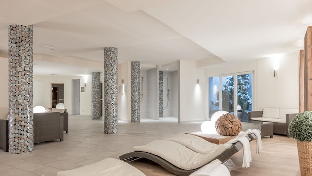 Un moderno espacio de spa con pilares de mosaicos, sillones de descanso y un amplio ventanal con vistas al exterior.