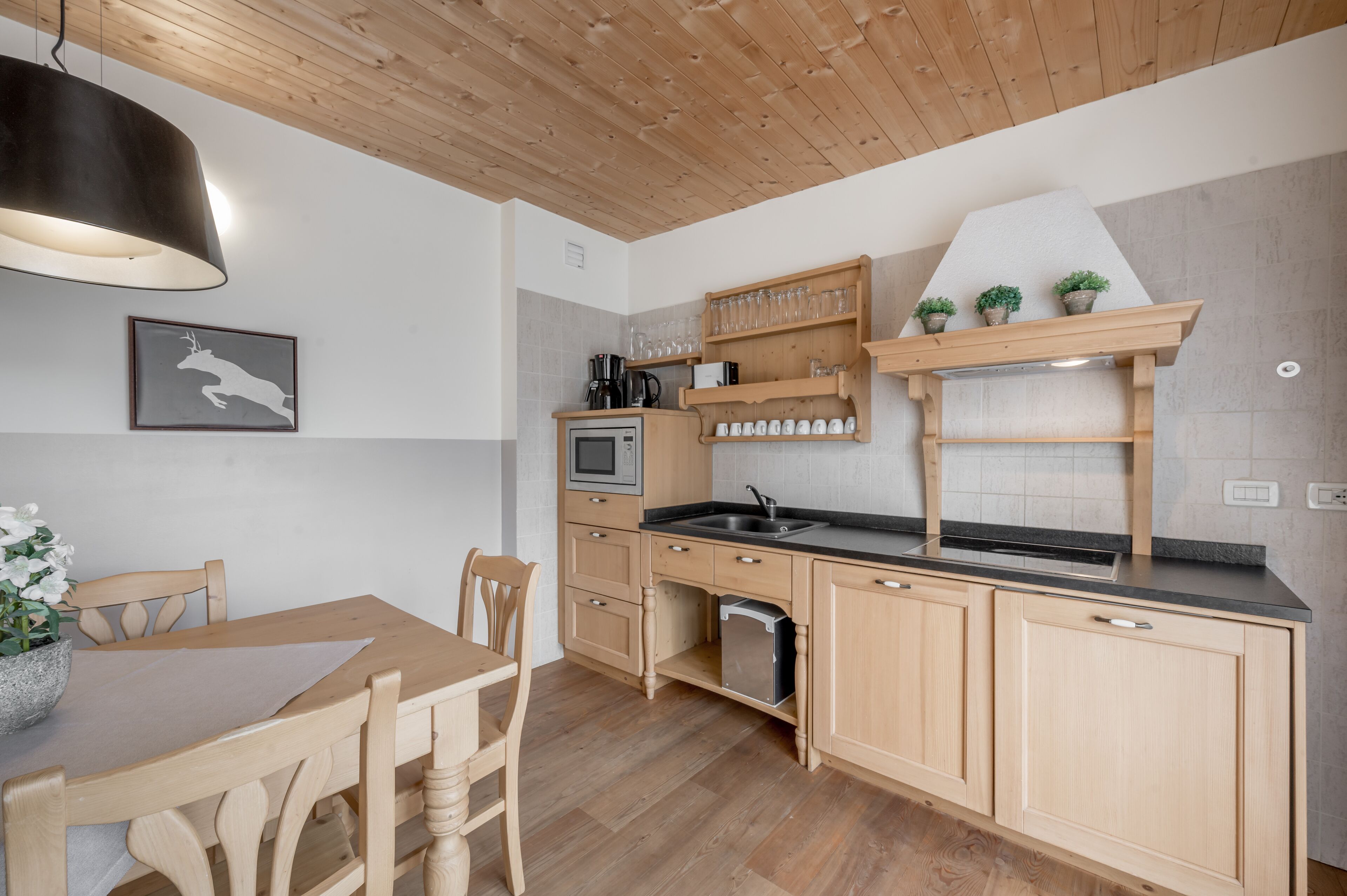 A modern kitchen with wooden cabinets, a built-in oven, and a sink. There is a dining table with chairs and a pendant light above it.