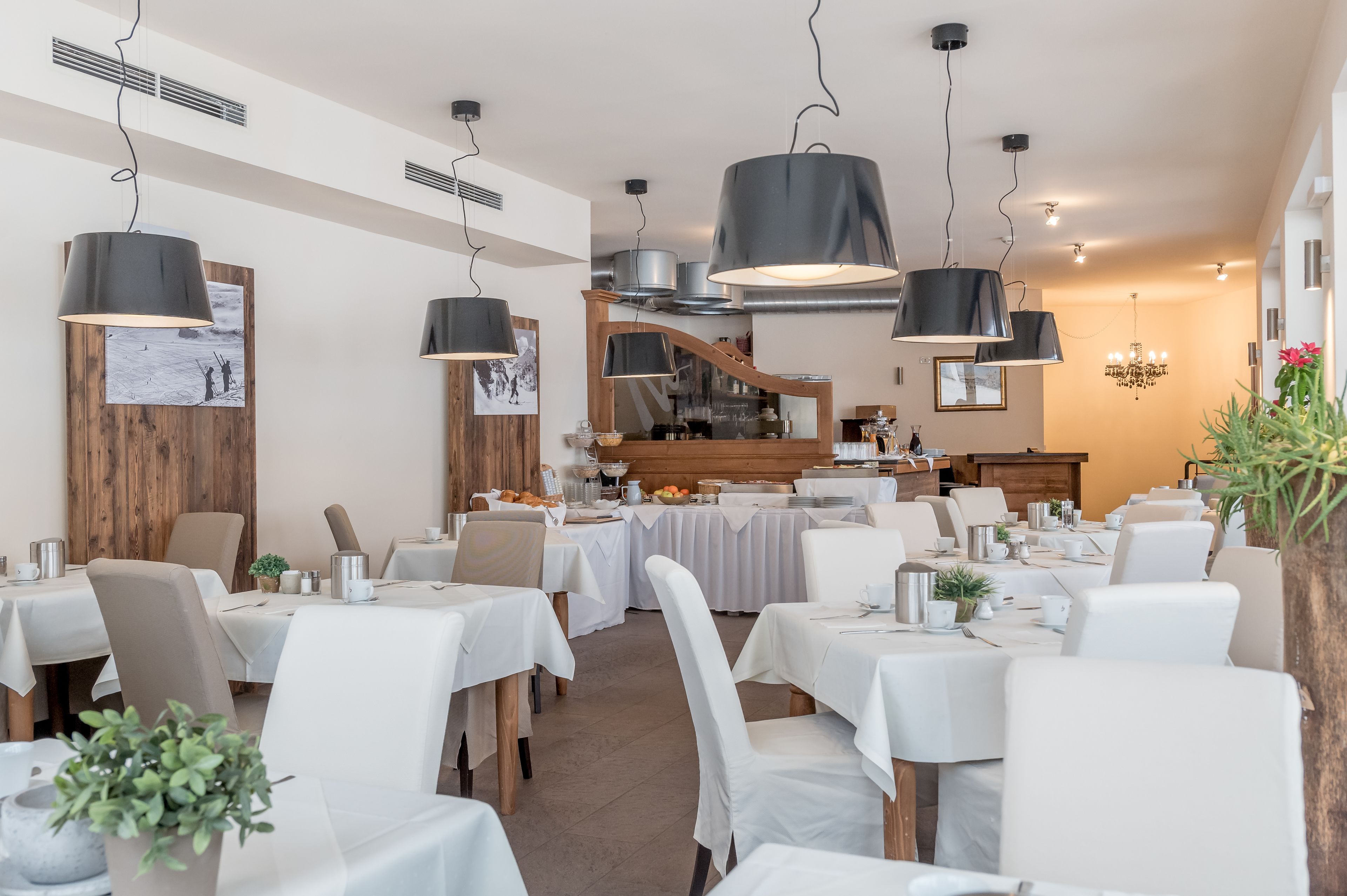 A restaurant with white tablecloths, black pendant lights, and a wooden accent wall.