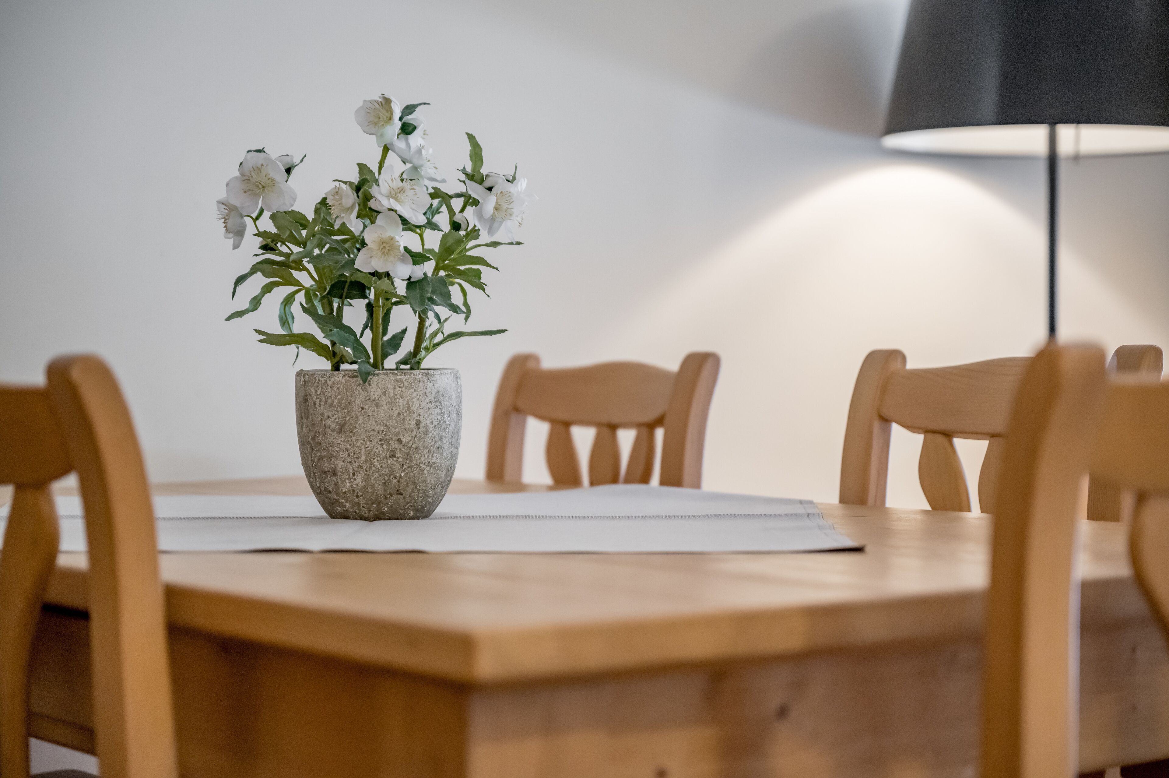 Una mesa de comedor con un jarrón de piedra que contiene flores blancas, rodeada de sillas de madera.