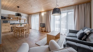 Un espacio habitable moderno con techo de madera, una zona de comedor con mesa y sillas de madera, un sofá gris y un televisor sobre un mueble.