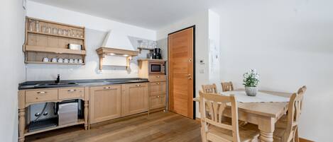 Cozinha compacta com armários de madeira, micro-ondas e uma mesa de jantar com cadeiras.