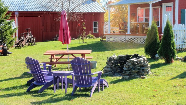 Un granero rojo, una mesa de picnic con sillas y un muro de piedra en un patio cubierto de césped.