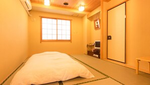 Een traditionele Japanse kamer met tatami vloerbedekking, een futon, een schuifdeur en een klein tafeltje met een stoel.