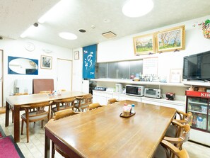 Un coin repas avec des tables et des chaises en bois, un four à micro-ondes, un réfrigérateur et un téléviseur posé sur une étagère.