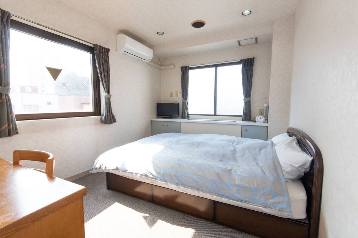 Een hotelkamer met een bed, een bureau, een televisie en een raam met gordijnen.