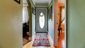 Un passadís amb una catifes estampada, una porta amb un finestral i una finestra amb cortines.