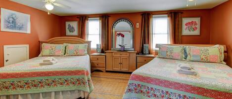 A bedroom with two beds, a dresser, a mirror, and a ceiling fan.
