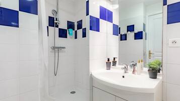 Un bagno moderno con piastrelle bianche e blu, una doccia, un lavandino con specchio e una pianta in vaso.