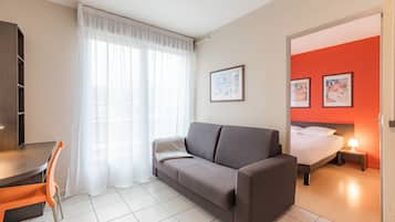 Ein modernes Hotelzimmer mit einer Couch, einem Esstisch mit Stühlen, einem Bett mit Nachttisch und Bildern an der Wand.