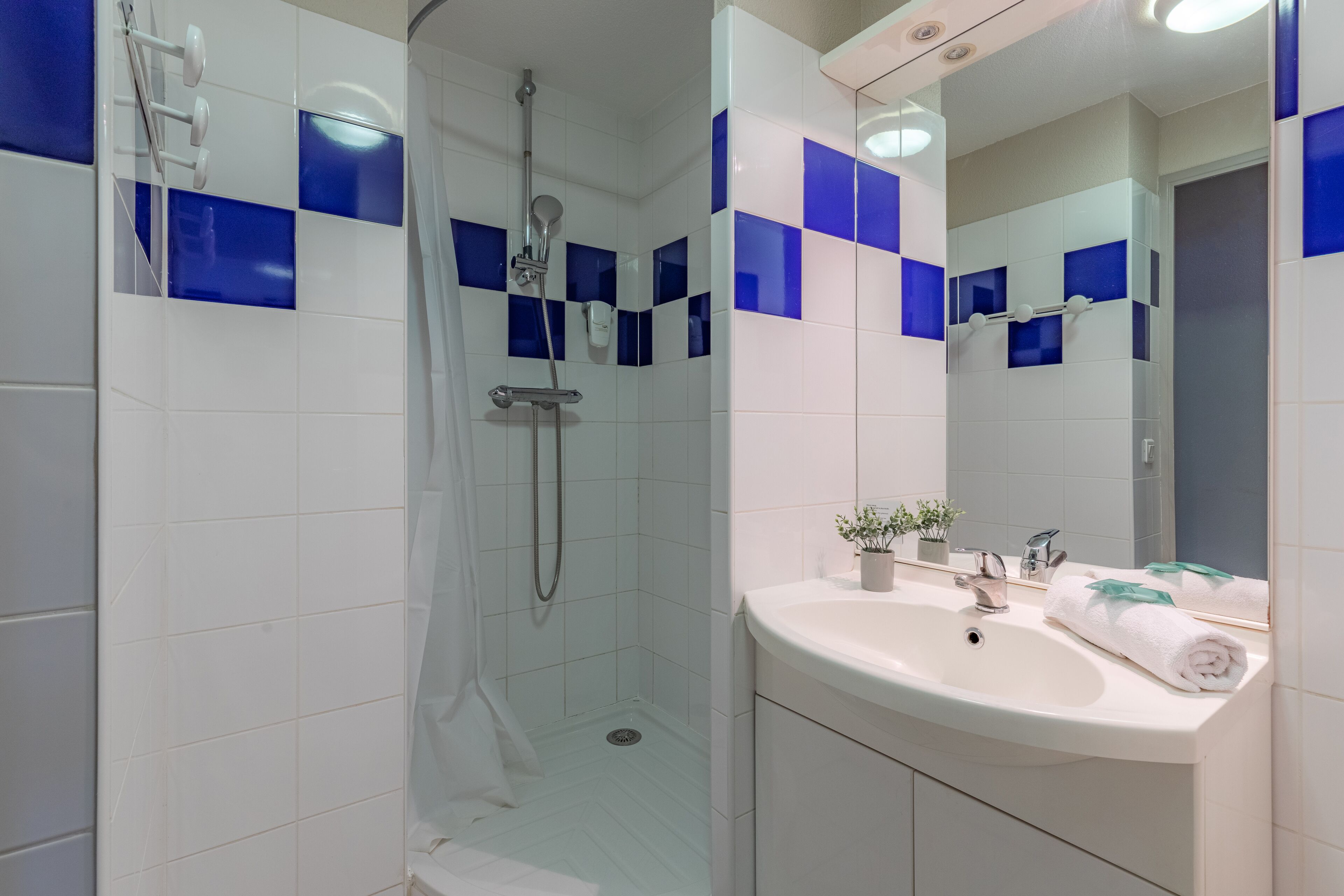 Un baño moderno con ducha envuelta en vidrio, un lavabo blanco con espejo y paredes de azulejos azules.