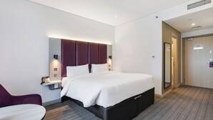 Moderni hotellihuone, jossa on suuri sänky, työpöytä, tuoli ja erillinen oleskelualue.