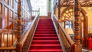 Una imponente escalera con alfombra roja y barandillas de madera que conduce a un piso superior.