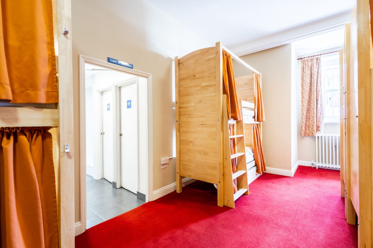 A room with a red carpet, a wooden bunk bed with a ladder, a white radiator, and a door leading to a bathroom.
