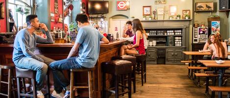A bar area with stools and tables, a counter, and a television mounted on the wall.