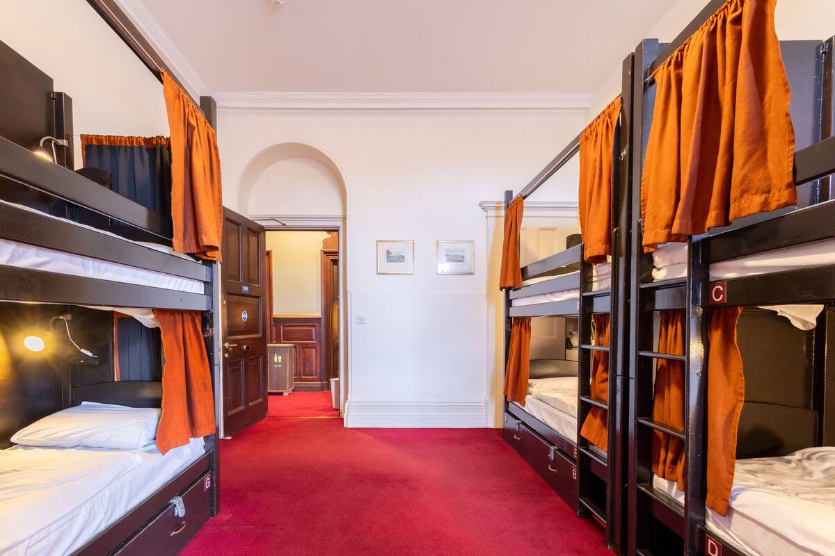 A hotel room with bunk beds, a red carpet, and a hallway leading to a door.