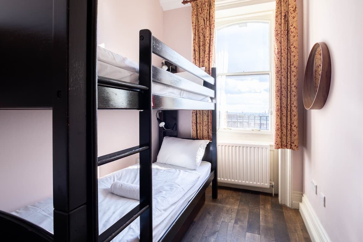 A bunk bed room with a window, curtains, and a radiator.