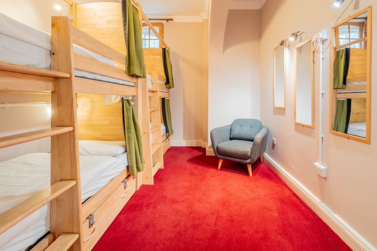 A room with bunk beds, a grey armchair, and a red carpet.