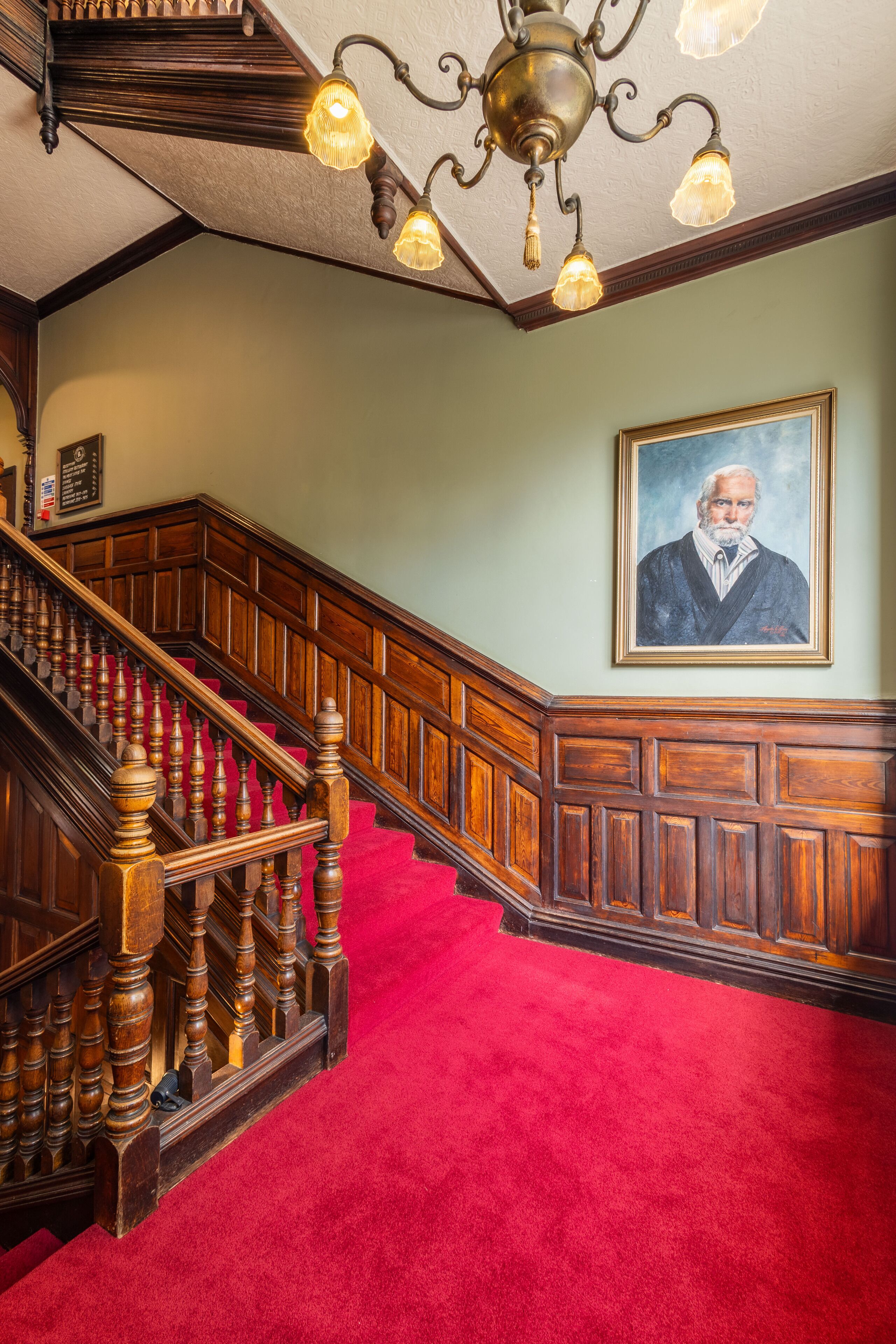 A grand staircase with a red carpet, wooden balustrades, and a chandelier.
