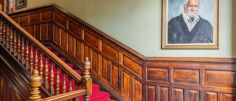 A grand staircase with a red carpet, wooden balustrades, and a chandelier.