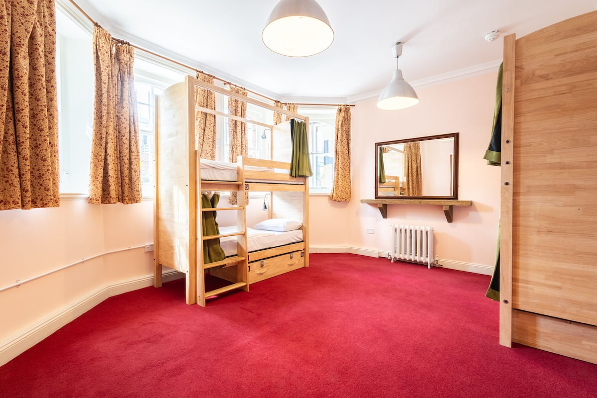 A room with a bunk bed, a radiator, a mirror, and a wooden wardrobe.