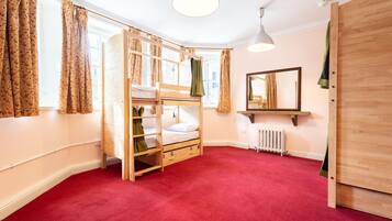 Une chambre avec un lit superposé, un radiateur, un miroir et une armoire en bois.