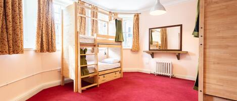 A room with a bunk bed, a radiator, a mirror, and a wooden wardrobe.