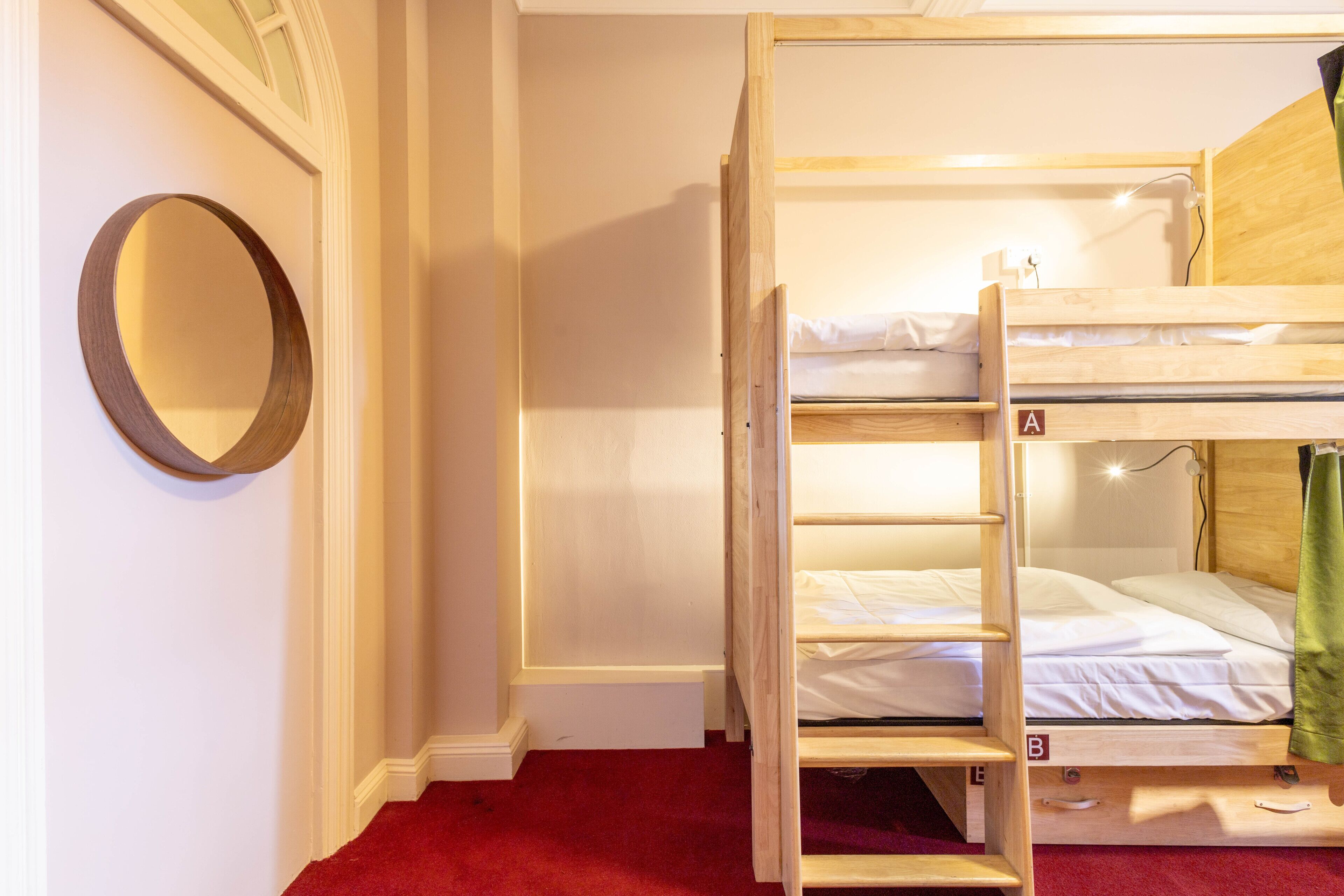 Een slaapkamer met stapelbed, een rood tapijt, een ronde spiegel en een houten hoofdbord.