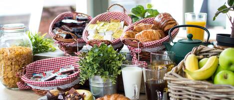 A breakfast table with various food items, including croissants, eggs, and fruits, along with beverages and a green kettle.