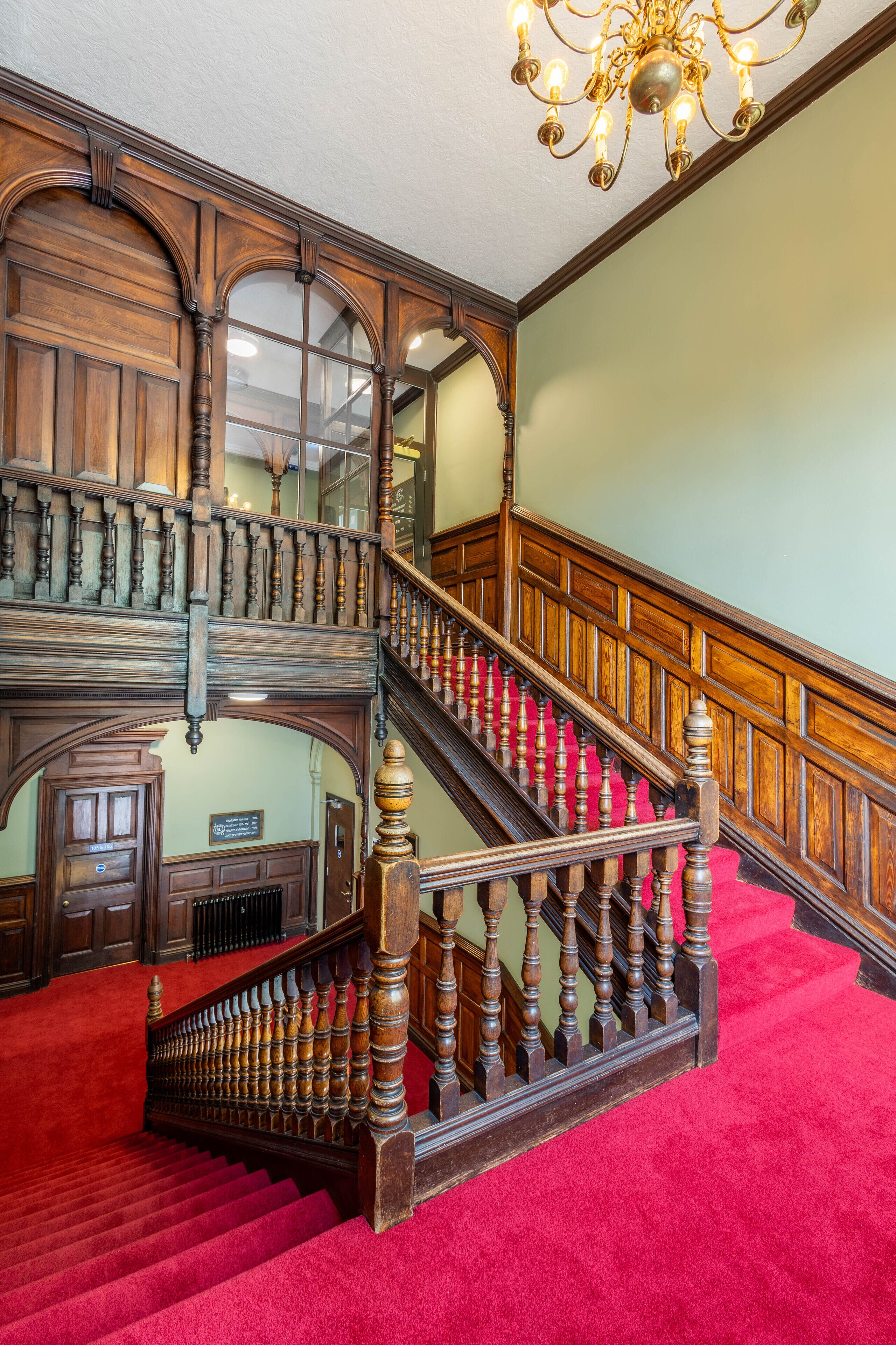 Un magnifique escalier orné de boiseries sculptées et recouvert d’un tapis rouge.