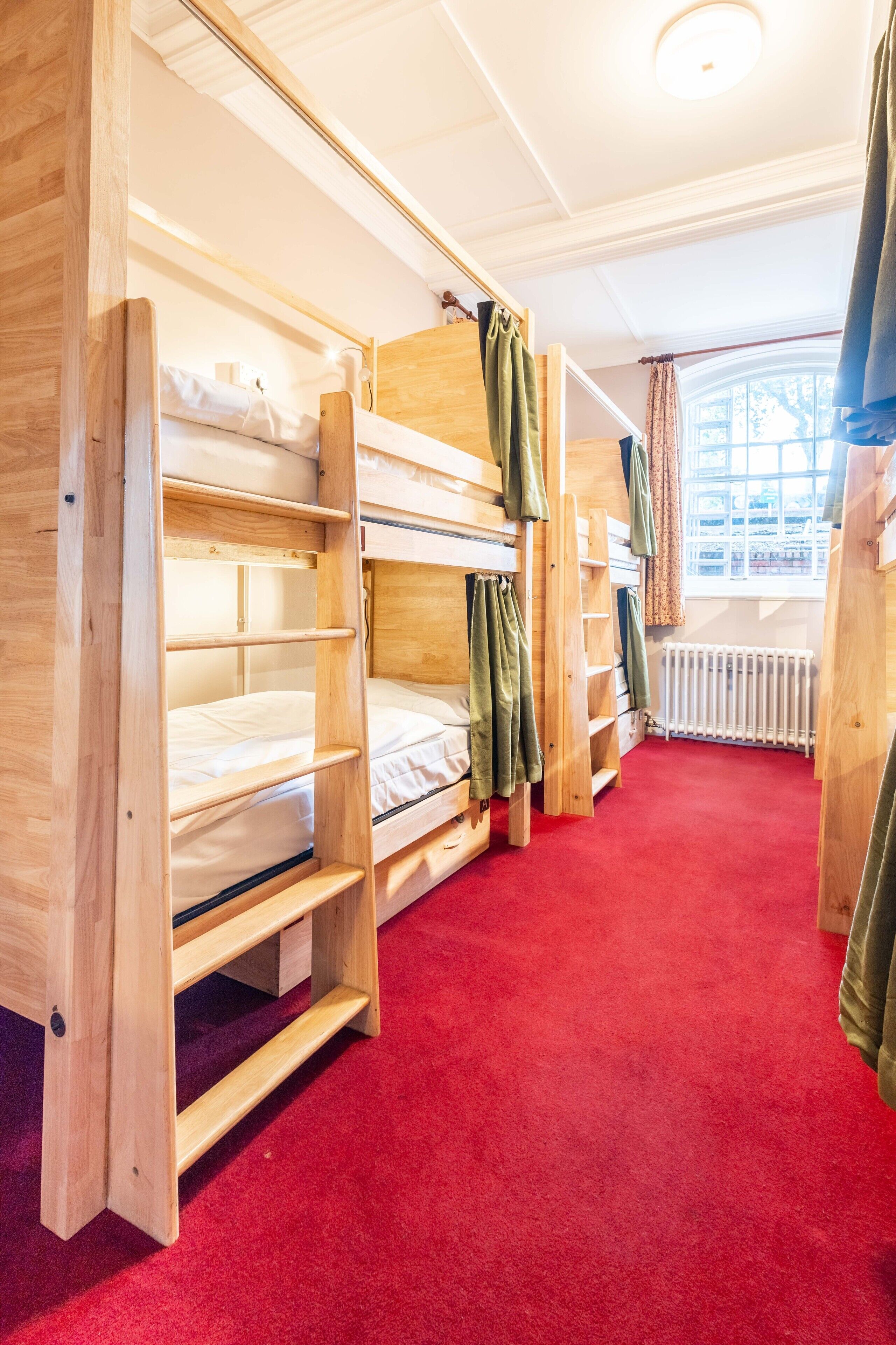 Ein Schlafraum mit Etagenbetten, einem roten Teppich, Holzwänden und einem Fenster mit Vorhängen.