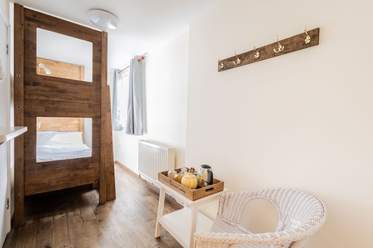 A cozy room with a wooden bed frame, a wicker chair, a small table with a tray of tea and snacks, and a wall-mounted coat rack.