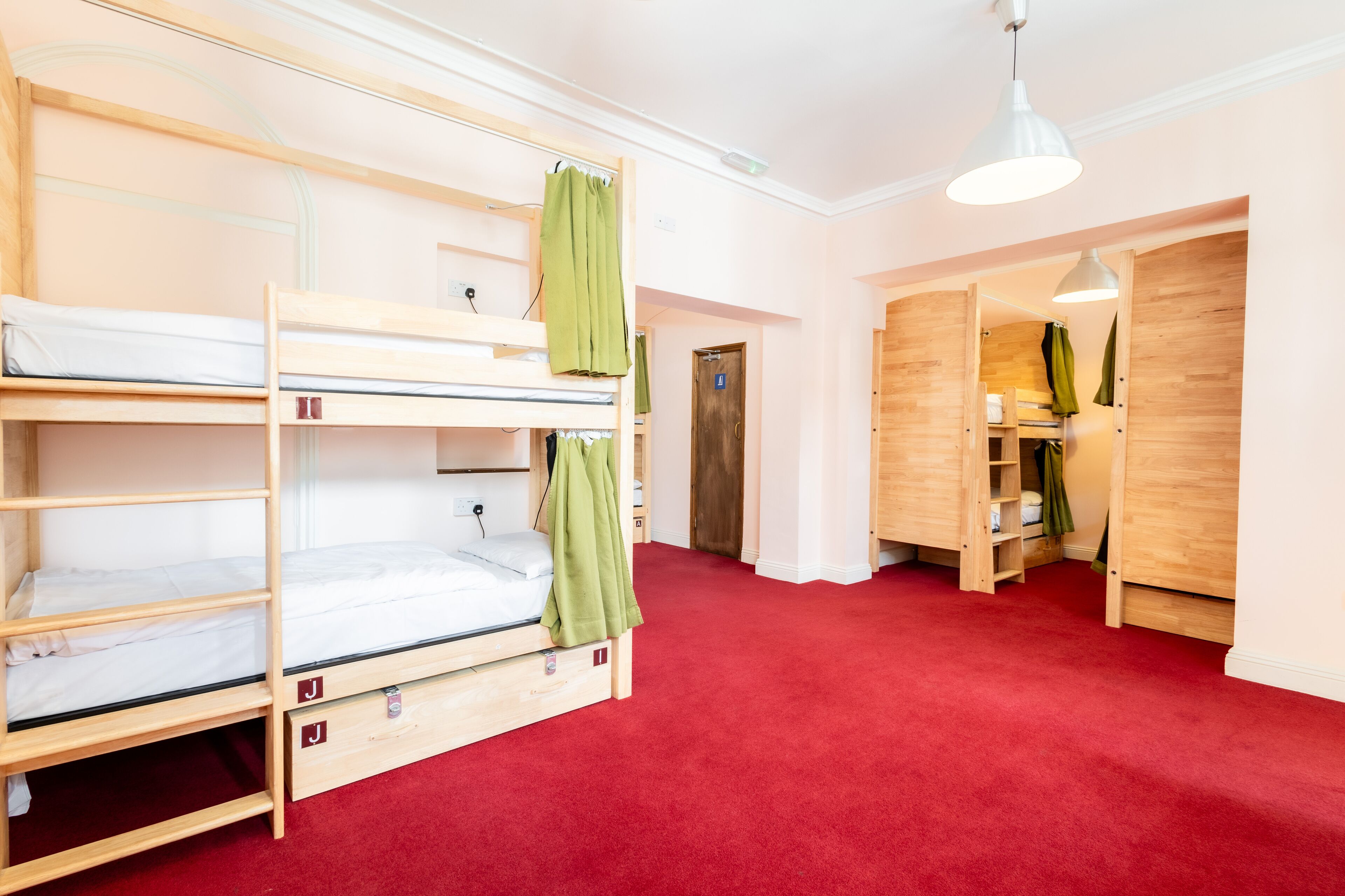 A dormitory room with bunk beds, a red carpet, wooden walls, and a hanging light fixture.