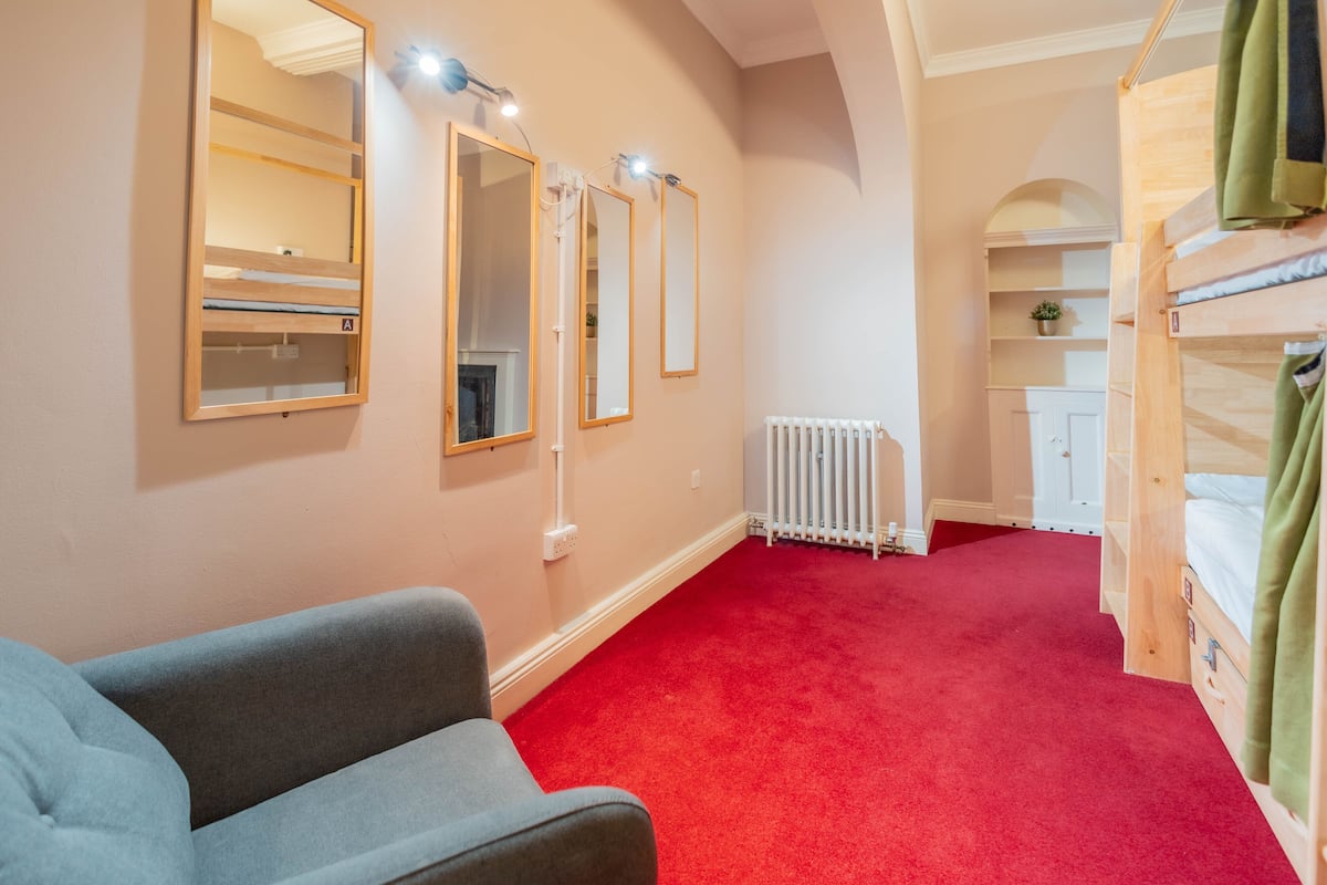 A room with a red carpet, a grey sofa, and a bunk bed with green curtains.
