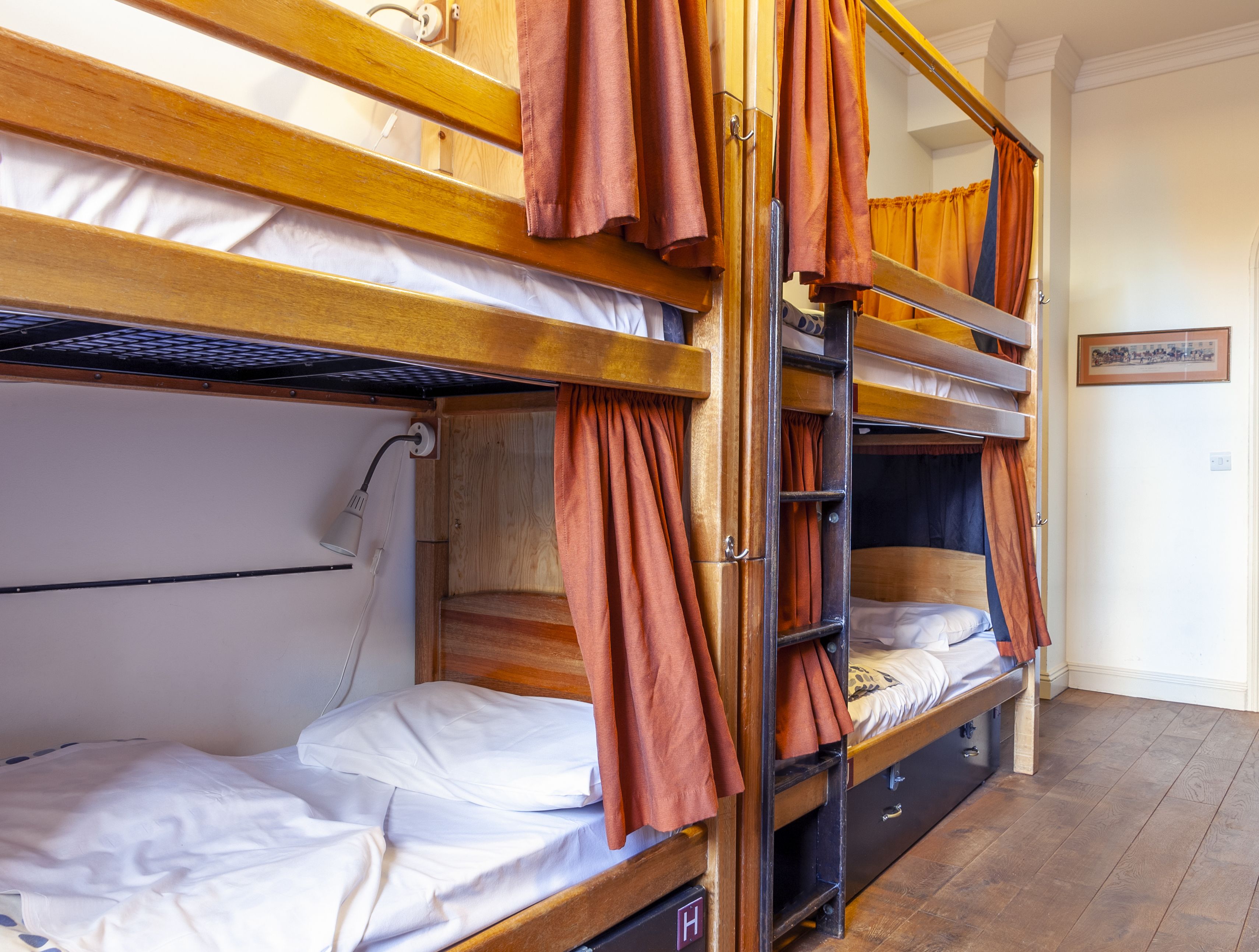A bunk bed room with wooden frames, a ladder, and orange curtains.