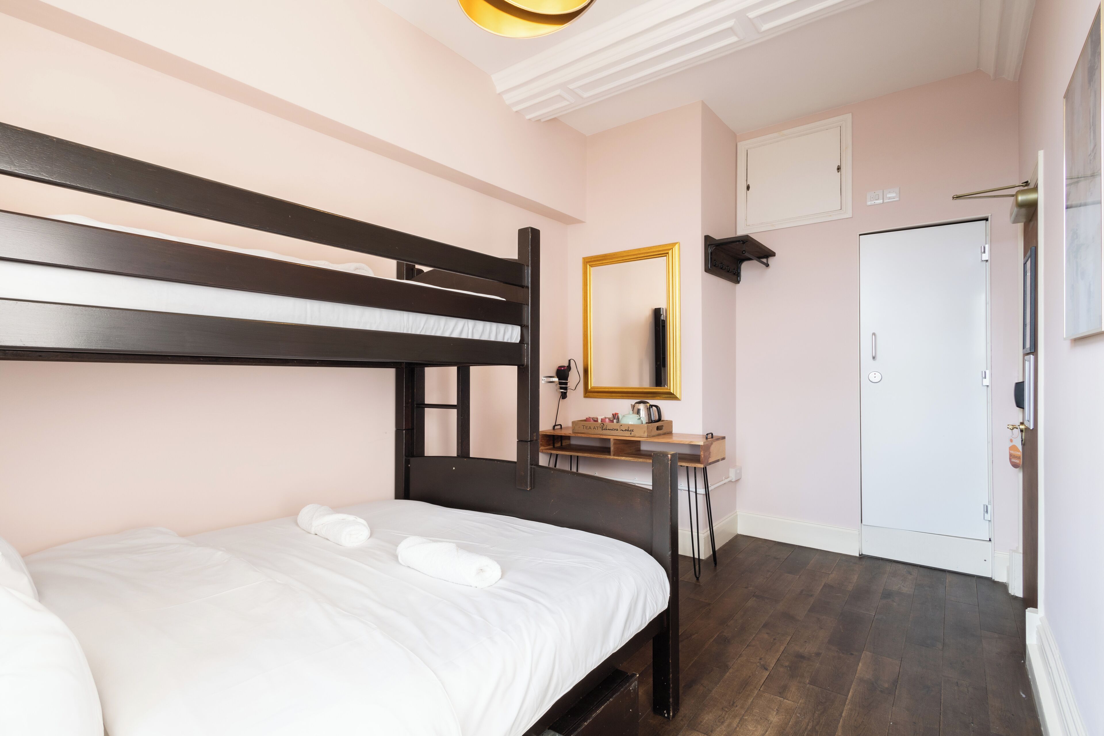 A bedroom with a bunk bed, a bedside table with a mirror, a dresser, and a door.