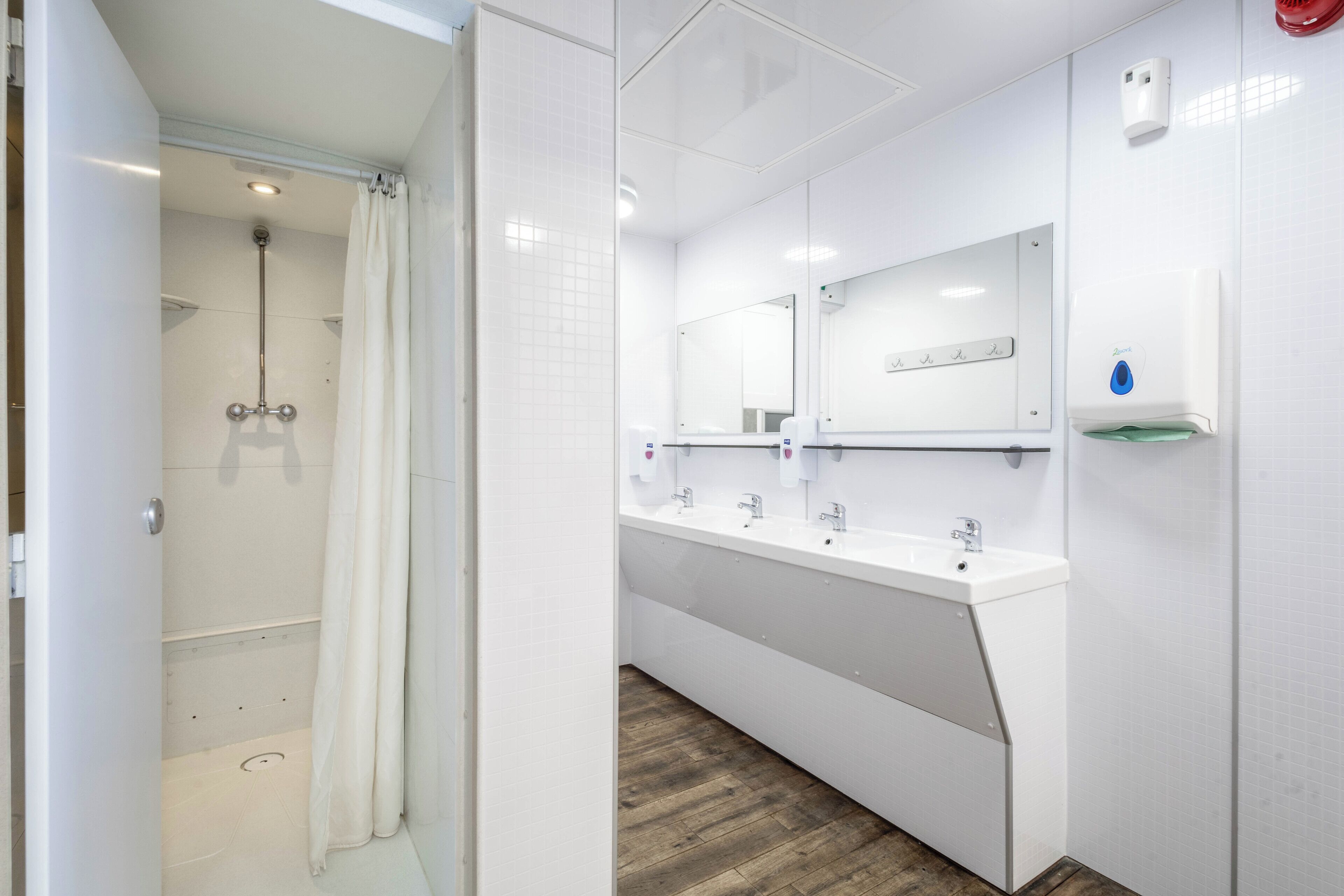 Un baño moderno con cabina de ducha, tocador con tres lavamanos y espejo sobre los lavamanos.