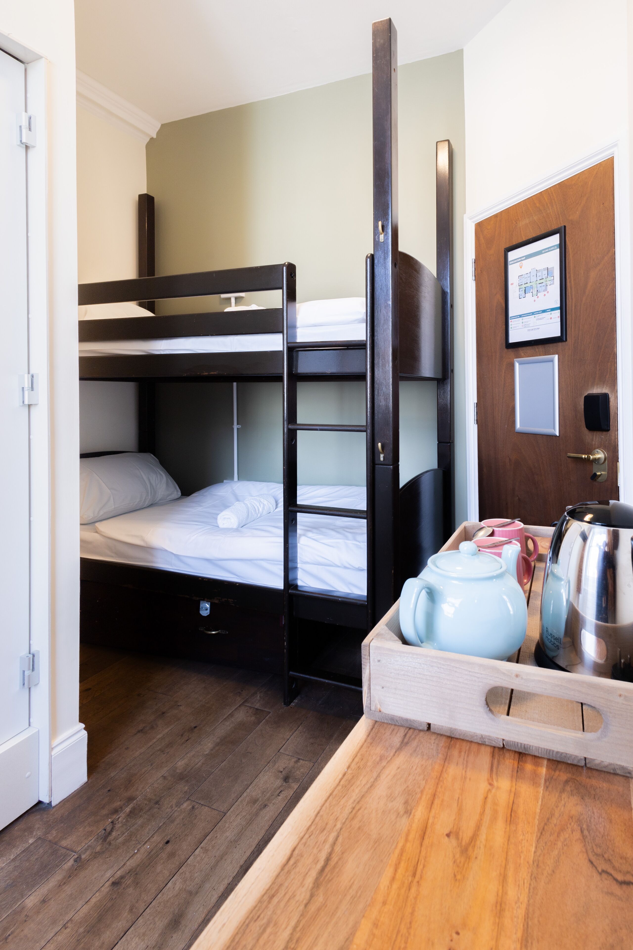 A bunk bed room with a wooden floor, a wooden door, and a tray with a teapot and cups.