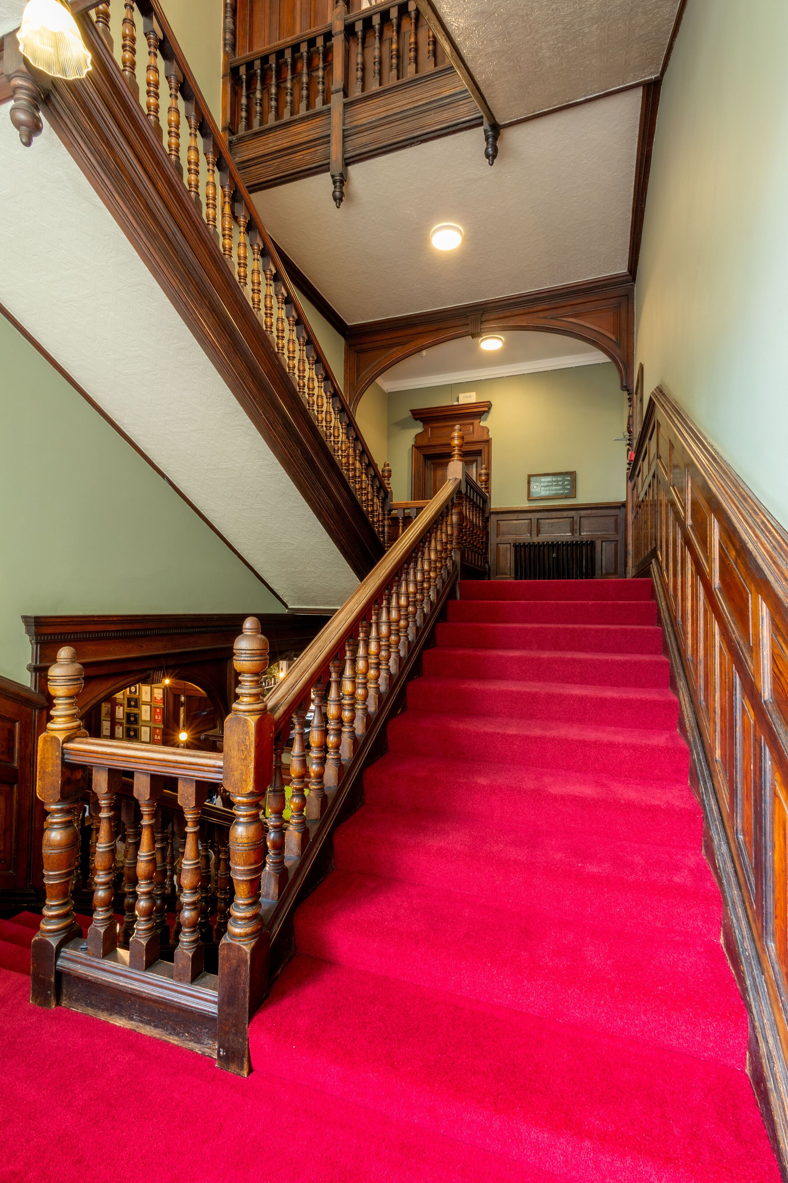 A grand staircase with ornate wooden balusters and a red carpet.