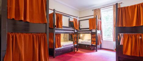 A room with bunk beds, orange curtains, and a red carpet.