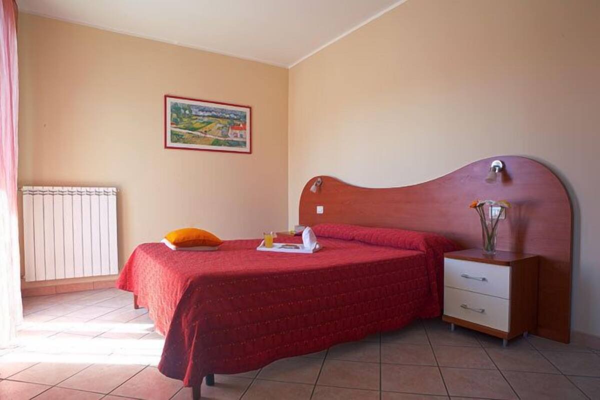 A bedroom with a bed, a nightstand, a radiator, and a painting on the wall.