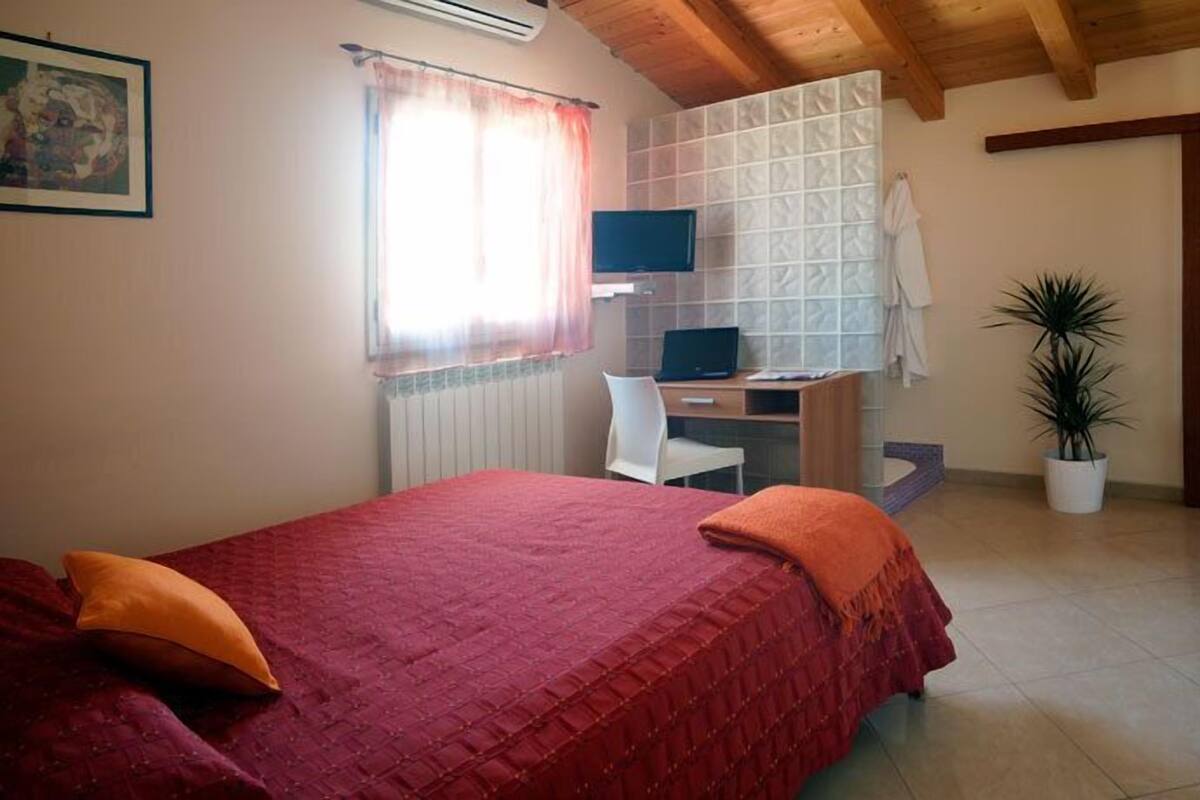 A bedroom with a bed, a desk, a chair, a television, and a potted plant.