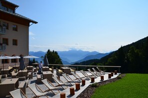 A terrace with lounge chairs and umbrellas, overlooking a mountainous landscape. - Hotel Norge (Trento)