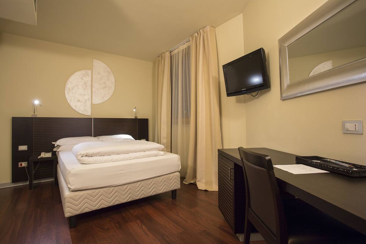 Hotellihuone, jossa on sänky, työpöytä, televisio ja peili.